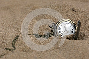 Round pocket watch on a chain in the sand