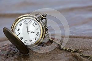 Round pocket watch with hands and a chain on the stone against w