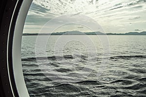 Round porthole on a cruise ship, interior view through the window on the coast and the sea, sunrise against the sea