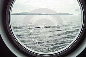 Round porthole on a cruise ship, interior view through the window on the coast and the sea, sunrise against the sea