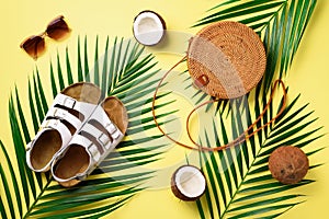 Round rattan bag, coconut, birkenstocks, palm branches, sunglasses on yellow background. Banner. Top view with copy