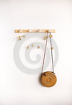 Round rattan boho crossbody bag hanging on wooden hanger against white wall indoors