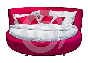 Round red bed with pillows and white toy bear isolated on white