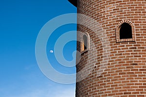 Round red brick block tower with round window in blue clear sky