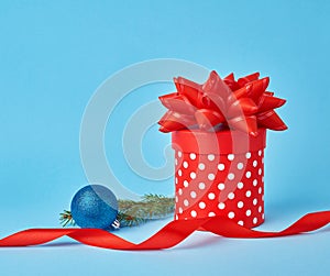 Round red cardboard box in white polka dots with a bow, sprig of spruce with a shiny blue ball