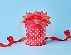 Round red cardboard box in white polka dots on top of a bow on a blue background