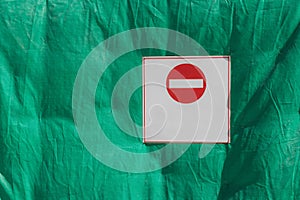 Round red and white `Do not enter` stop sign on a plate against a green background.