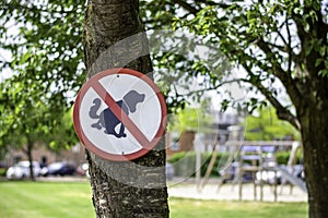 Round red and white no dogs poop zone sign in front of children playground in a neighbourhood