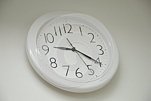 A round rounded white wall clock showing a quarter pass nine