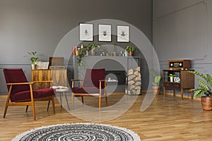 Round rug in front of red armchairs in grey retro living room in