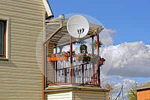 Round satellite dish on an open balcony with flowerpots and flowers on a private house