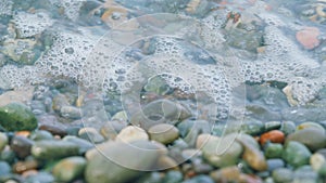Round Sea Pebbles Are Washed By Clean Transparent Sea Waves. Small Sea Foam Waves. Close up.