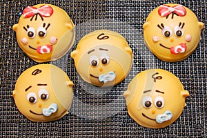 Round-shaped cookies of yellow color in the form of smile children`s faces on the background of a brown lattice. Confectionery