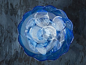 Round shaped ice cubes in a glass dark blue vase on a gray background for cooling drinks