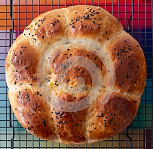 Round share and tear traditional home cooked Jewish Challah bread loaf, presented on a wire tray, topped with nigella seeds.