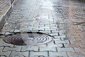 Round steel sewer manhole on wet cobblestone road