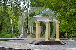 Round stone gazebo in the shape of a rotunda on a wooden pedestal in the park