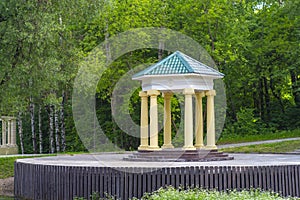 Round stone gazebo in the shape of a rotunda on a wooden pedestal in the park.