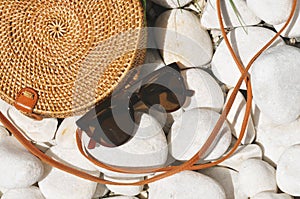 Round straw bag with black sunglasses on pebble stones