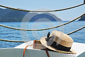 Round straw bag and straw hat on a lounge chair with blue sea, mountains and sky on the background
