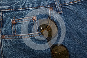 Round sunglasses on a denim texture background. round yellow glasses in the front pocket of jeans. Rough denim material. Classic