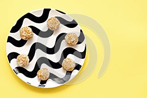 Round sweets. Energy balls in coconut flakes on a black and white plate on a yellow background. healthy food sports