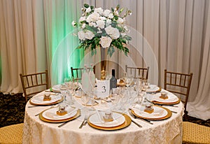 Round table in a restaurant decorated with white roses and empty golden plates waiting for guests photo