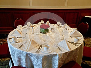 Round table set for wedding reception with white damask tablecloth, and red roses flower arrangement