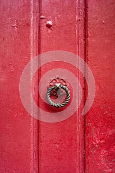 A round and twisted cast iron door knocker fitted on an old wooden door painted in red