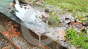 Round view of drain and trough under eaves. Leaves and sand brink by water flows away.