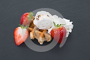 Round waffle decorated with ice, strawberry and cream laying on