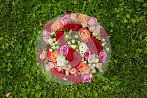 Round wedding bridal bouquet of red, yellow and pink roses on a background of green grass. View from above. Center