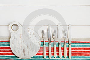 A round, white, battered cutting Board and antique eating utensils - knives and forks with bone handles. The Board and appliances