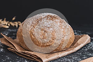 Round white bread on a paper bag on a black table.