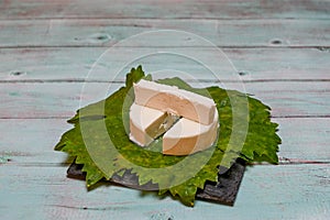 Round white homemade goat milk cheese on vine leaf on a wooden table