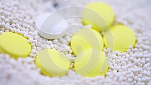 Round white pills fall on scattered white granules and yellow painkillers
