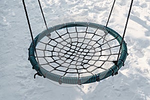 Round wicker swing seat for children on melted snow. Hanging rope swing near the house. place for relaxation and