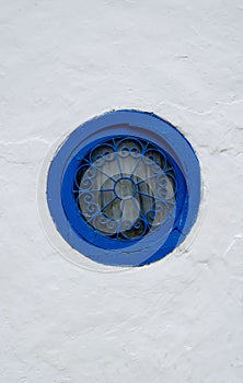 Round window with a blue frame with a patterned grille on a white wall
