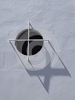 Round window with crossed bars on white concrete