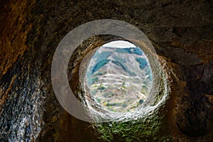 A round window in a sandstone cave with a view of the opposite mountain. Selective focus