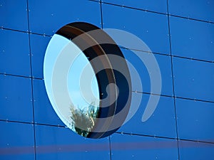 Round window on a wall covered with blue glass panels