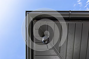 Round wireless camera mounted on the corner of the roof in the soffit, monitoring of a single-family house.