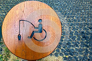 Round wooden handicapped fishing sign on shore of lake in public park