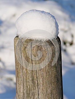 A round wooden posts of a wooden fence covered with snow cap