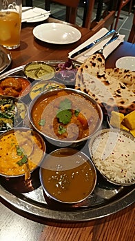 A round wooden tray filled with a variety of colorful Indian dishes. The dishes are arranged in a circle. In the center