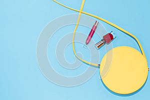 Round yellow purse, red nail polish, red lipstick on a pastel blue background.