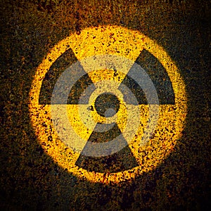 Round yellow radioactive ionizing radiation danger symbol painted on a massive rusty metal wall background