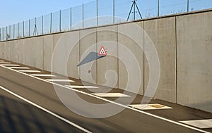 Roundabout warning triangle road sign, on concrete surrounding wall at the end of the higway.