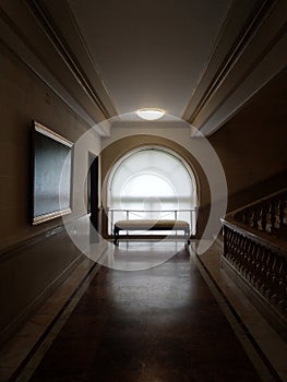 A rounded window with a bench at the end of a starcase hallway.