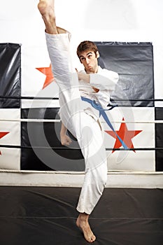 Roundhouse kick. Full length shot of a young martial artist practicing karate in the ring.